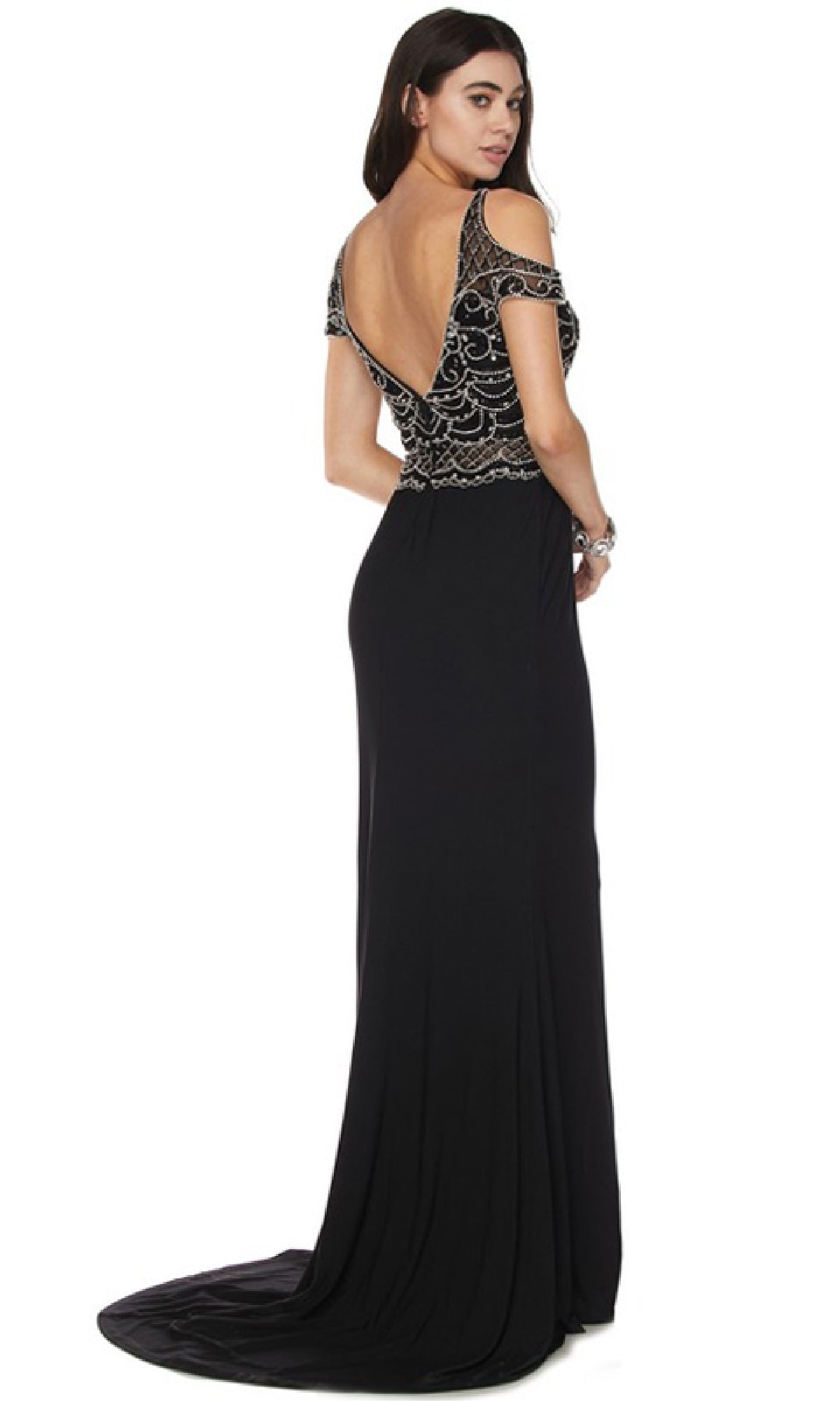 A woman stands with her back to the camera, wearing the Juliet 660 long prom dress featuring a floor-length, form-fitting silhouette, an open back, short sleeves, and a silver beaded bodice.